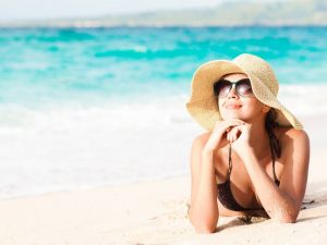 zaffy-mulher-deitada-na-praia-tomando-banho-de-sol-sorrindo-de-chapeu-oculos-escuros